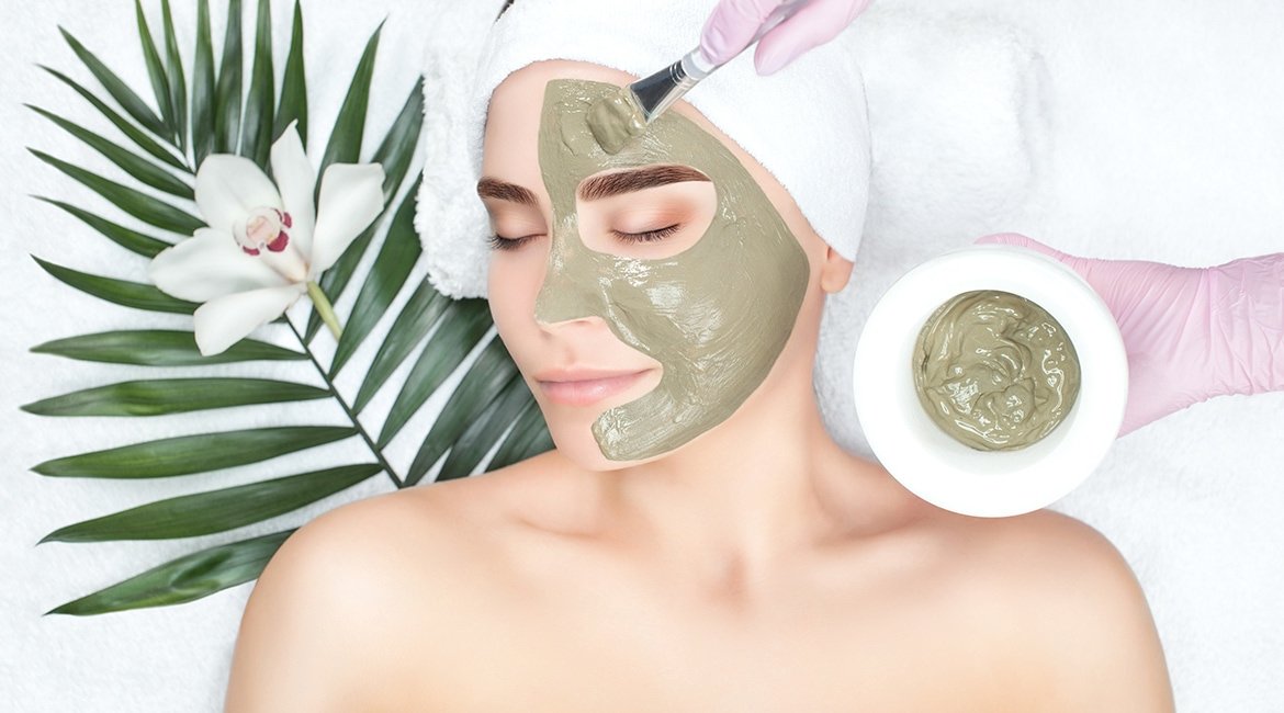 Lächelnde Frau mit Maske aus grüner Tonerde